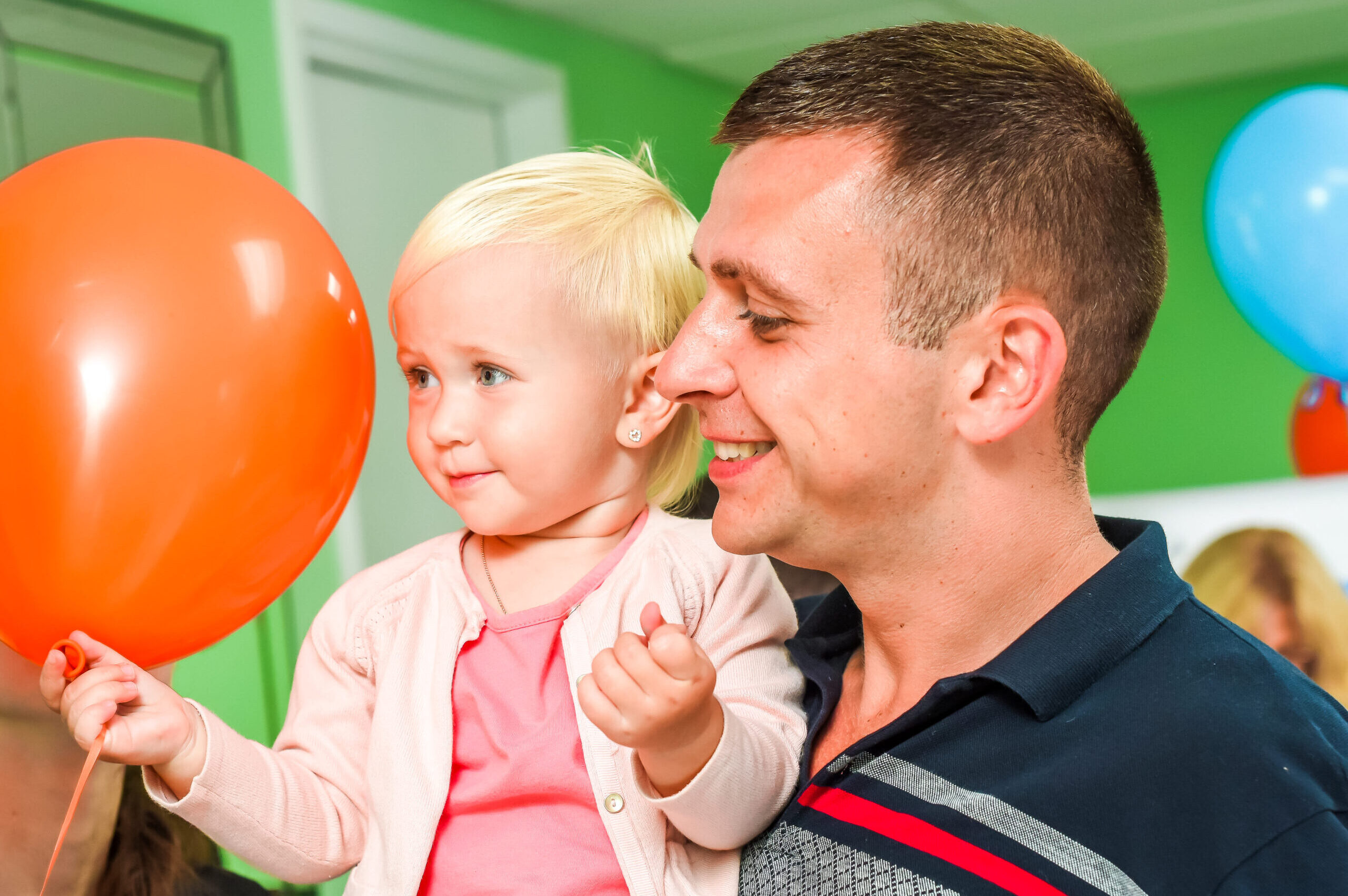 Child with a parent holding balloons at Little Scholars Daycare event