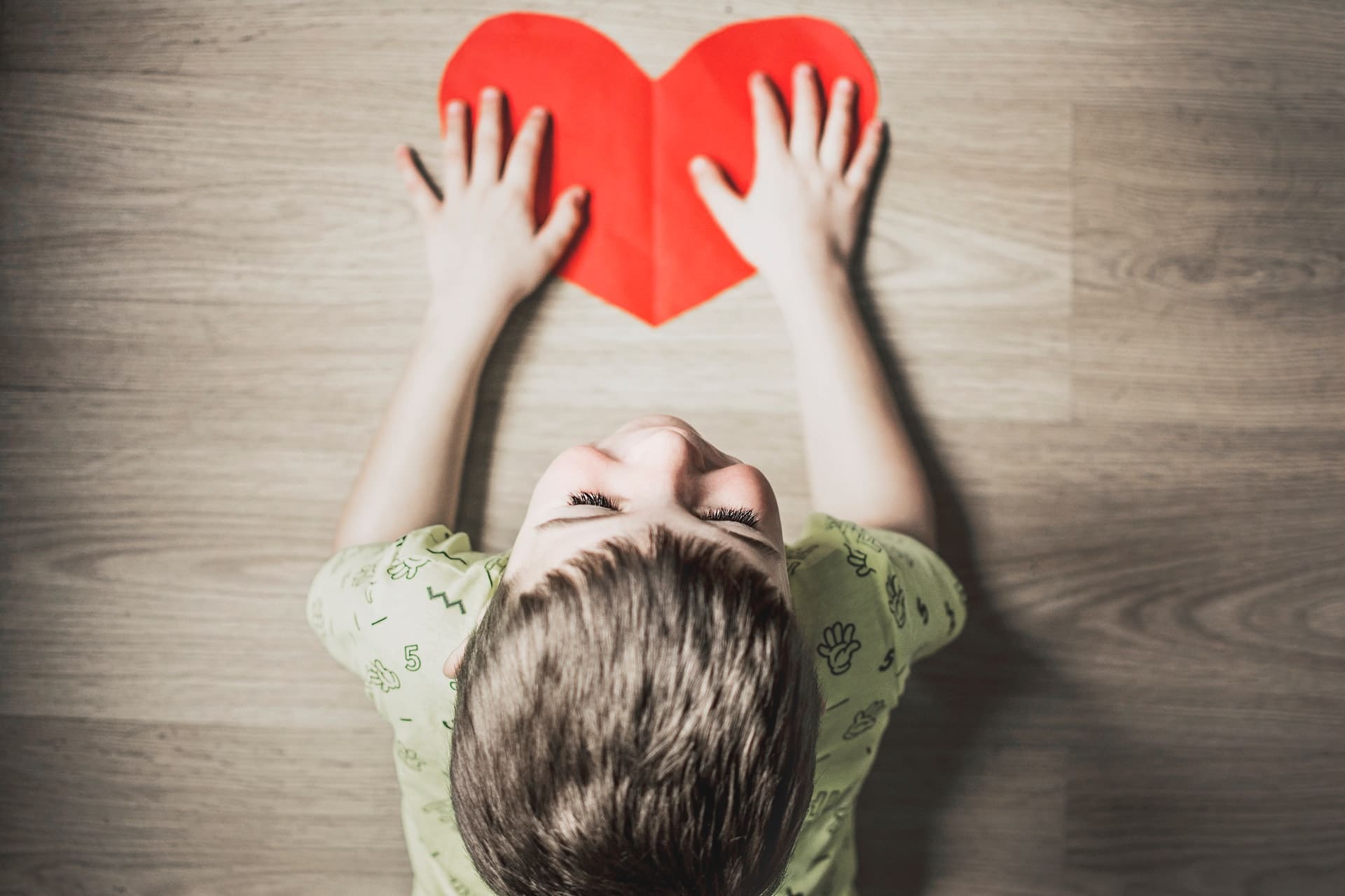 boy holding the heart shaped red paper lying on the floor
