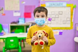 boy wearing the mask holds a teddy bear