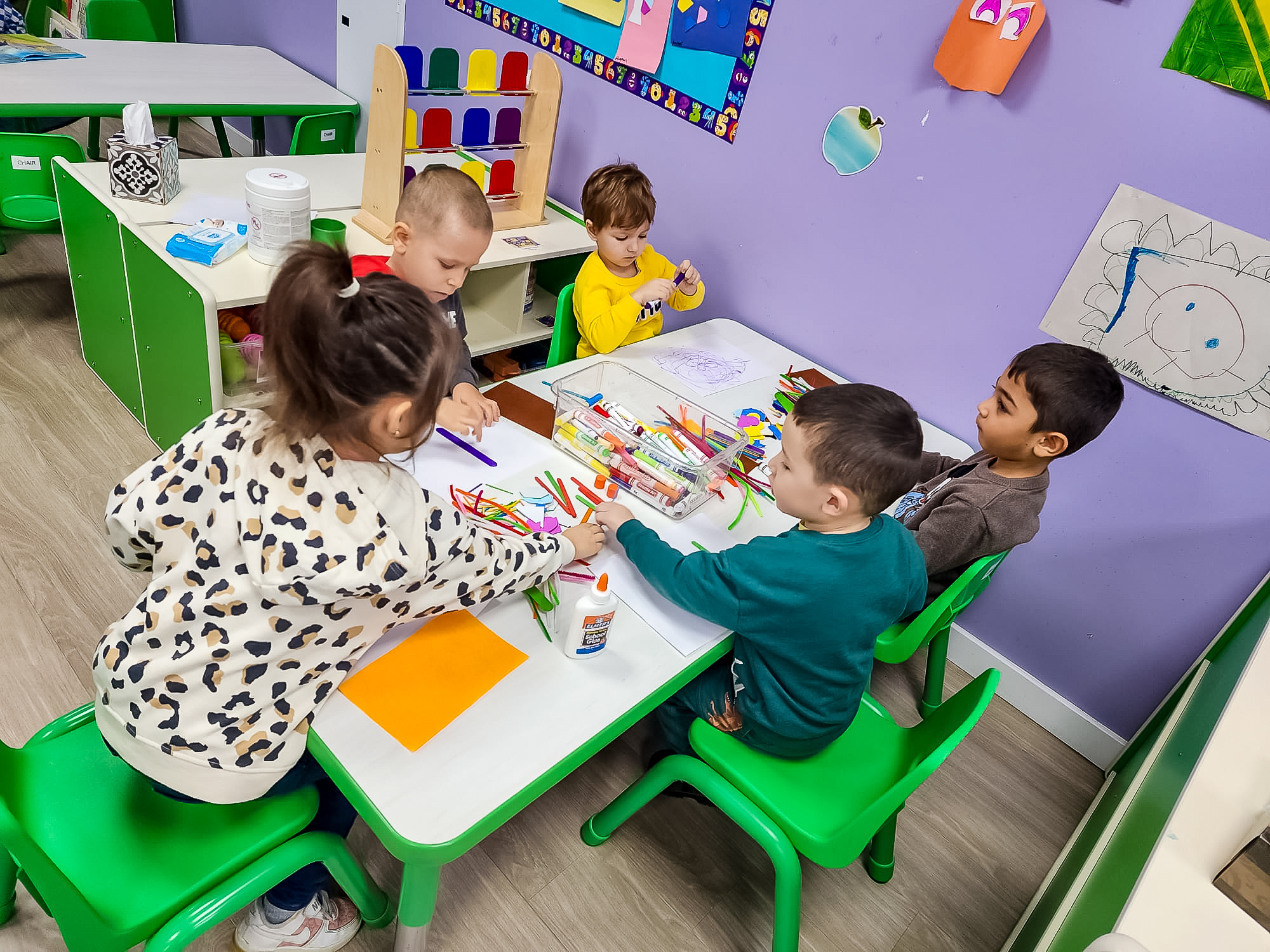 Children sit at the table on green chairs draw and glue