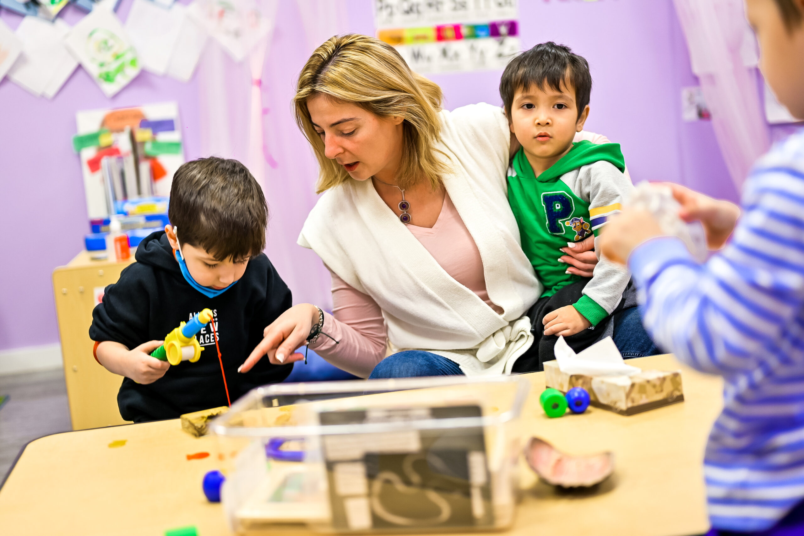 Woman with blond hair wearing pink and white clothes. Sitting next to two boys in Little Scholars Daycare