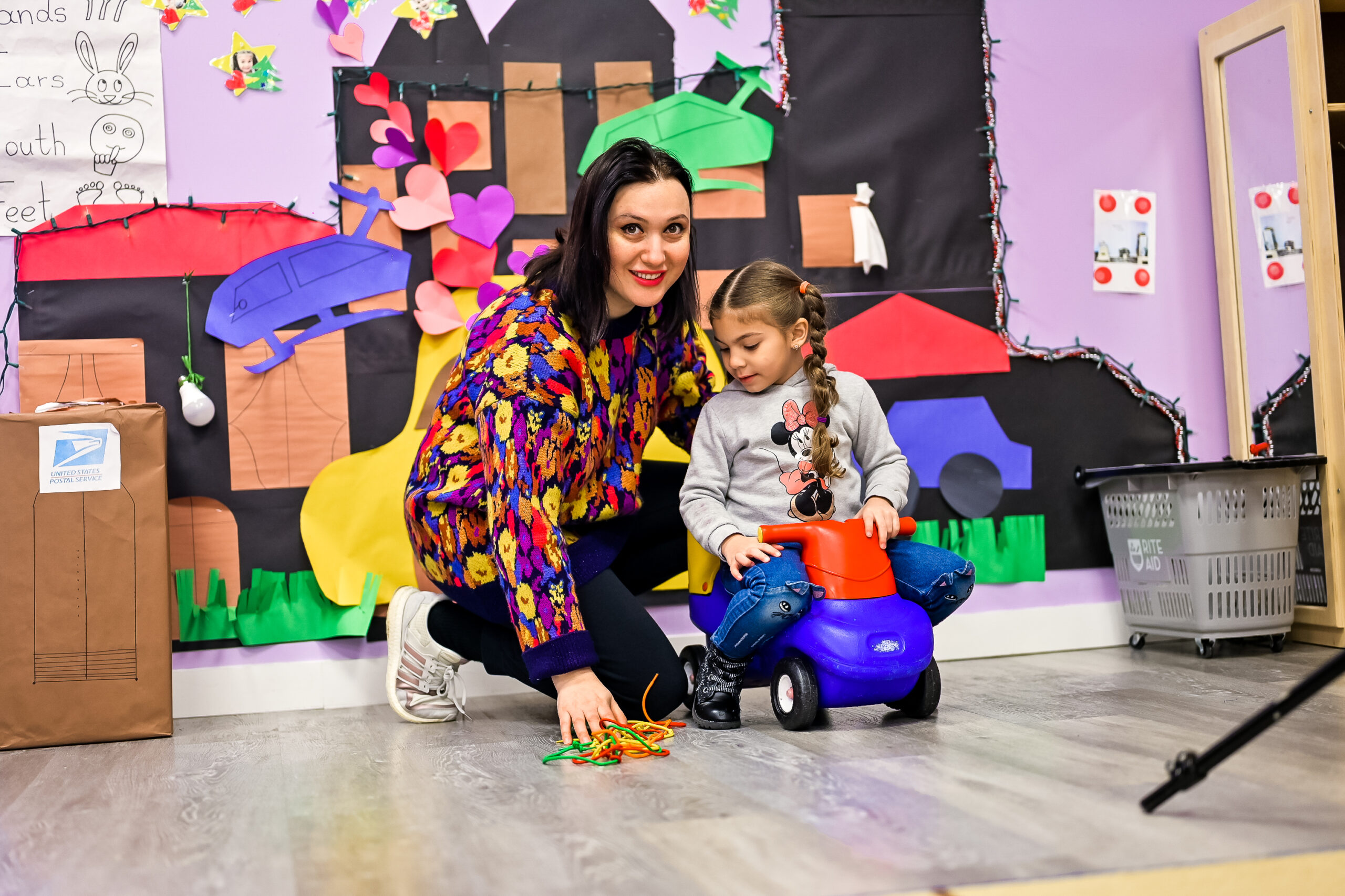 a woman with dark hair next to a child with a toy in kindergarten