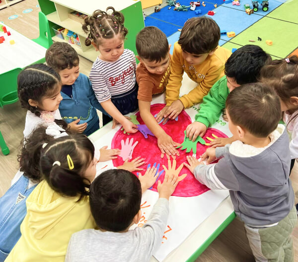 Group of diverse children engaging in a handprint activity on a large red paper in their daycare classroom