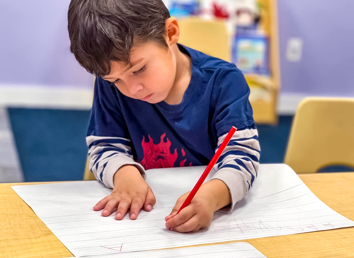 Child practicing writing skills with concentration at Little Scholars Daycare