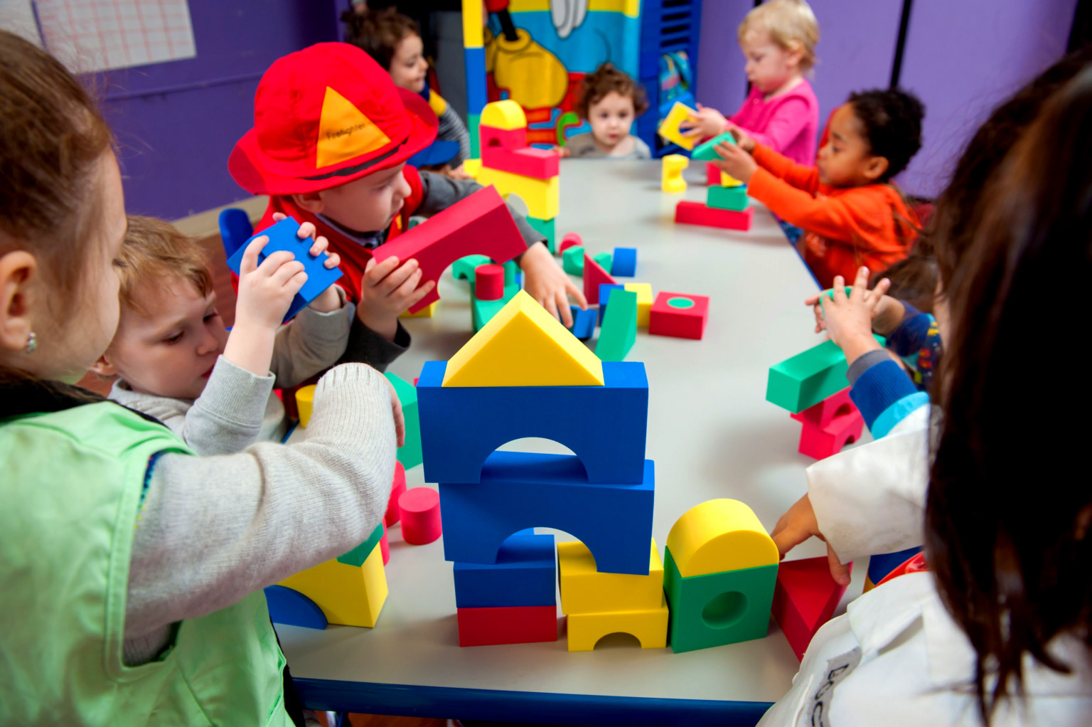 Group of children playing with colorful foam blocks at a table, building various structures in a classroom setting