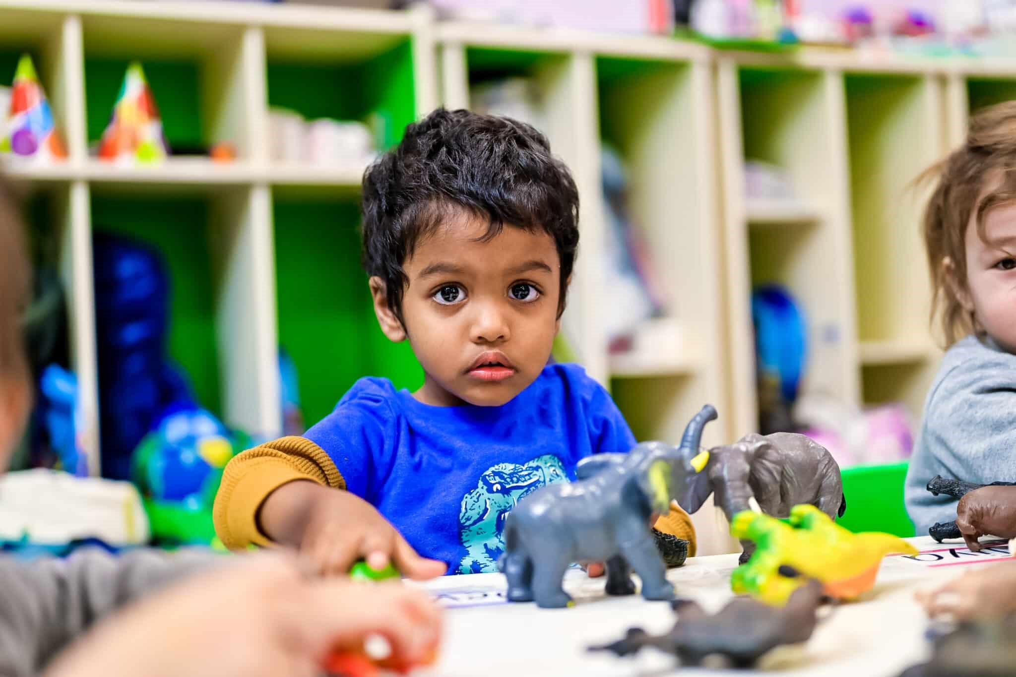 A young boy sitting at a table in a daycare classroom, playing with toy animals.