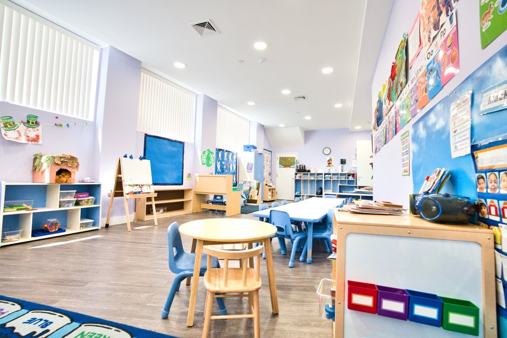 Spacious daycare classroom with various activity stations, small tables and chairs, and colorful educational posters on the walls
