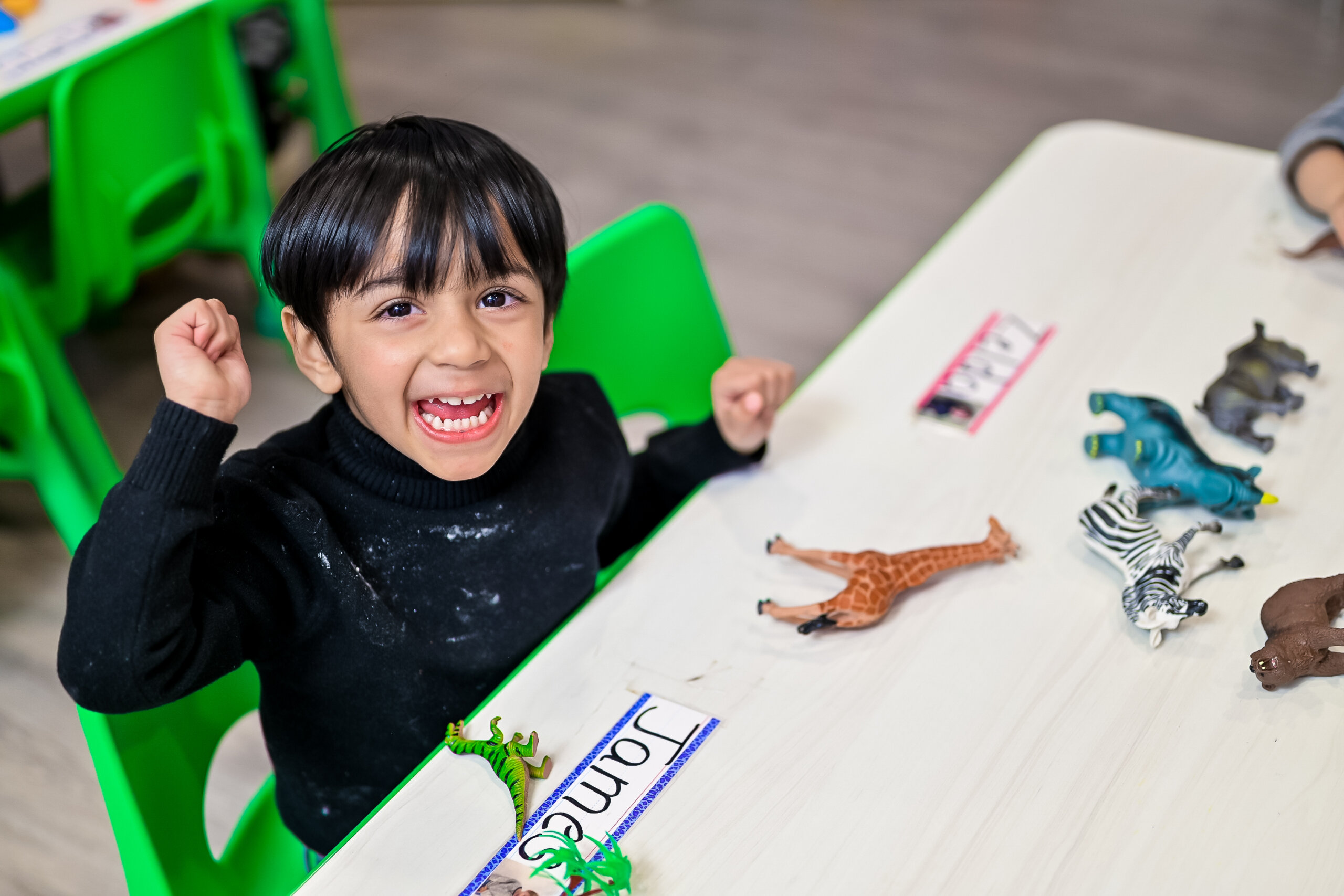 Excited young boy sitting at a table with toy animals in a daycare classroom