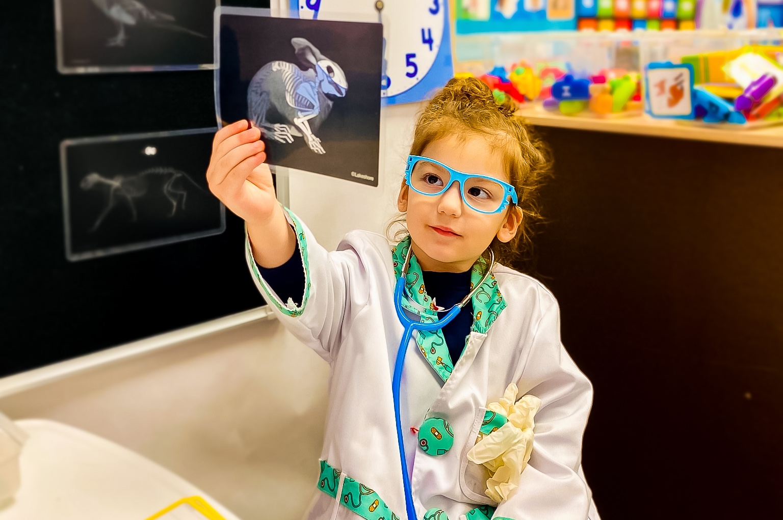 Young girl dressed as a doctor holding up an X-ray of a rabbit in a daycare classroom