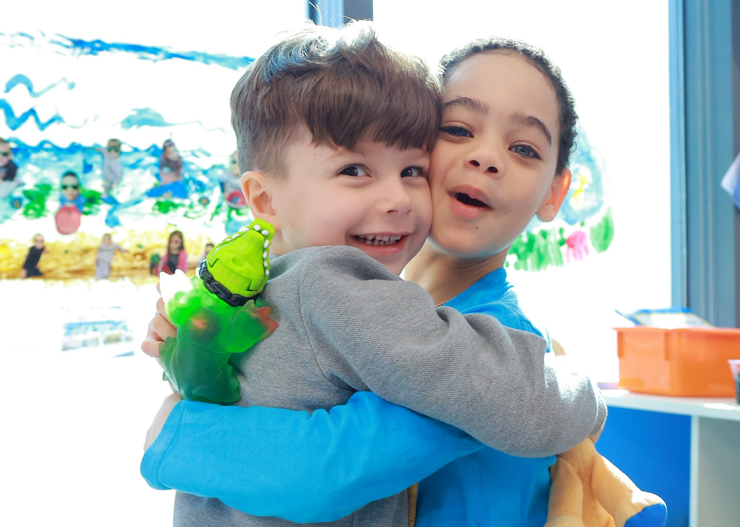 Two young children hugging and smiling in a brightly lit daycare classroom.