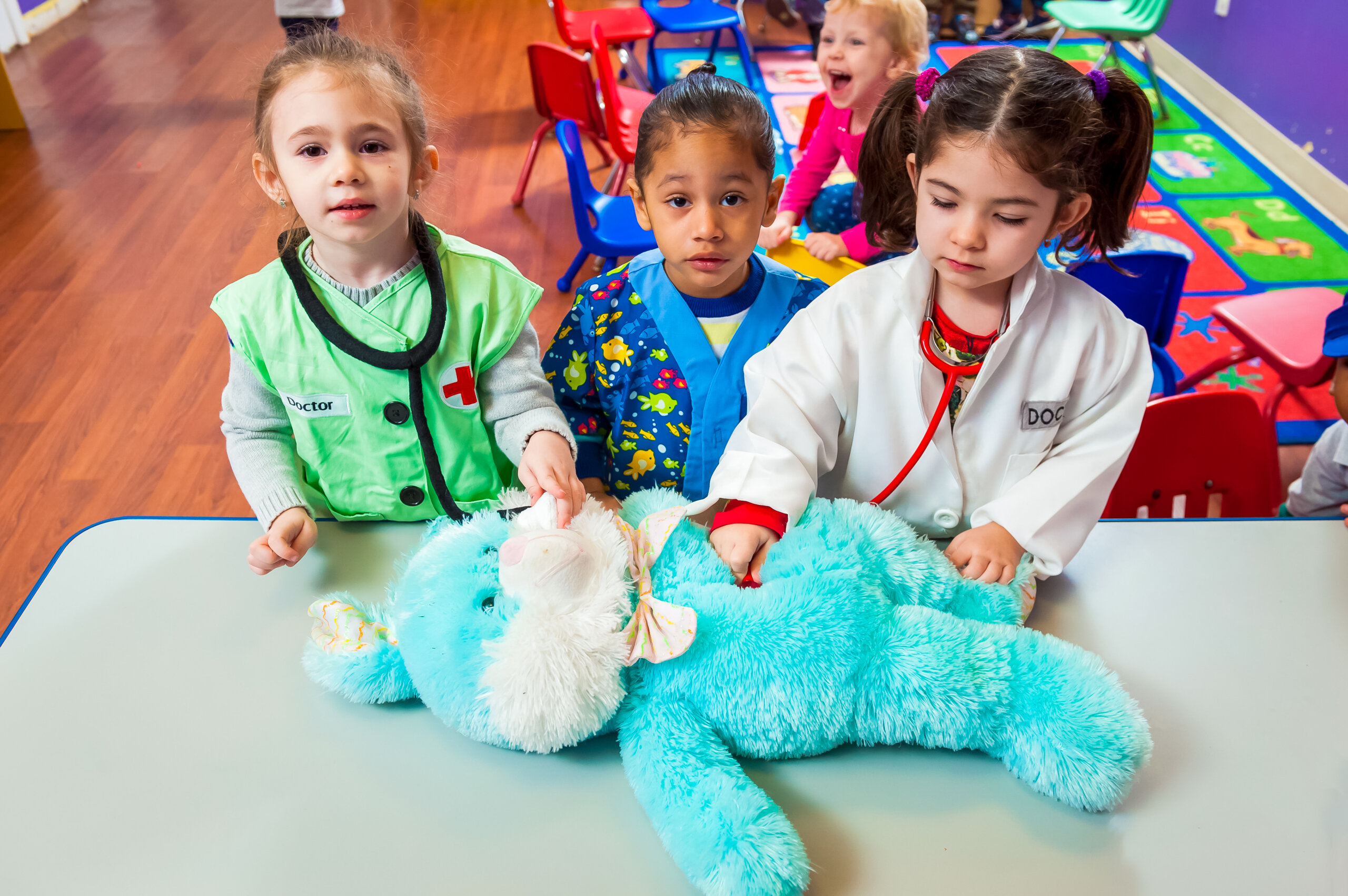 Three young children dressed in doctor's costumes playing with a large blue stuffed animal.