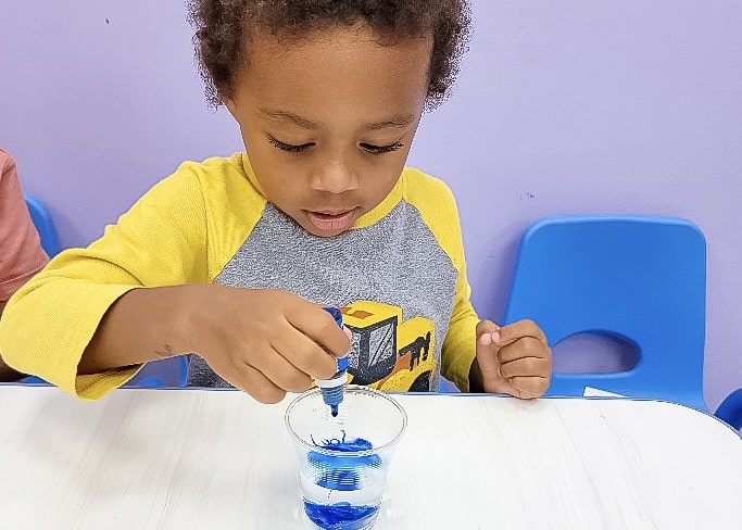 Young child adding blue food coloring to water for a simple color mixing science experiment