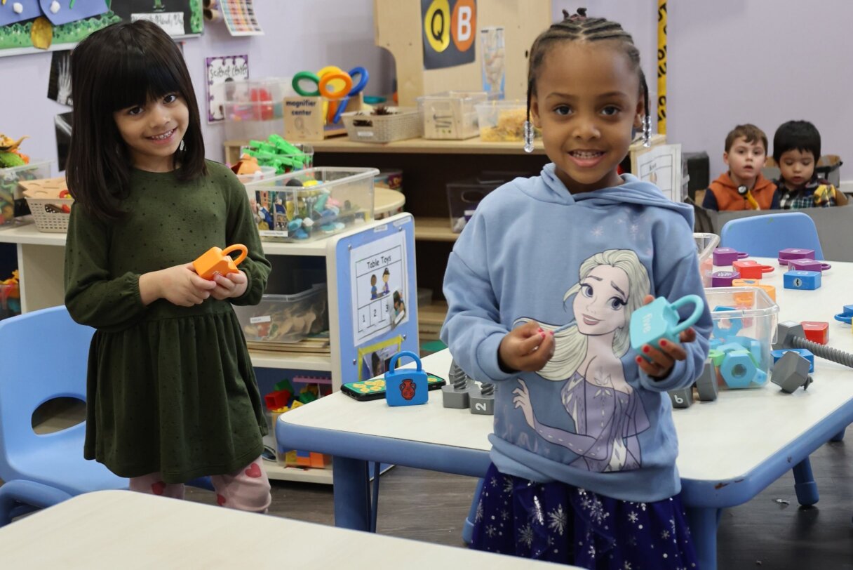 Two cheerful girls organizing and sorting toys as part of a classroom clean-up activity