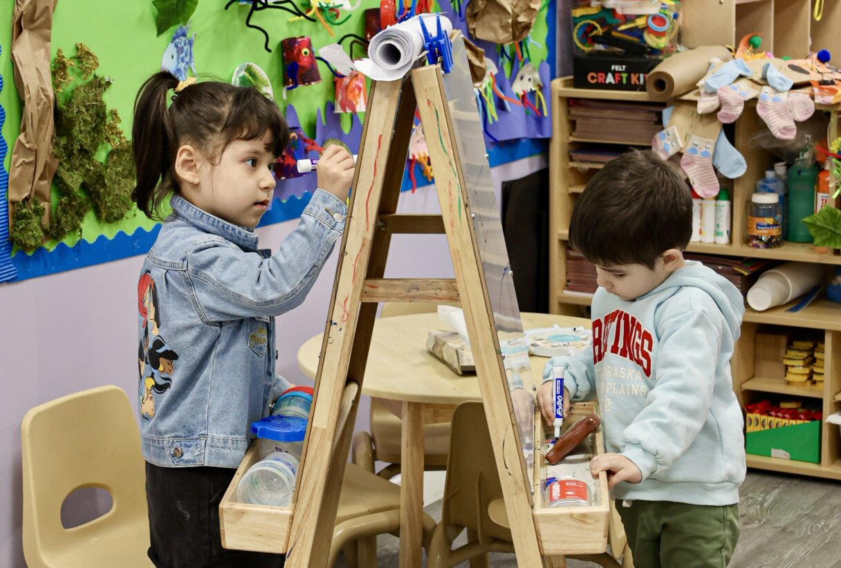 Two children focused on painting with eco-friendly materials on wooden easels for a spring craft project.