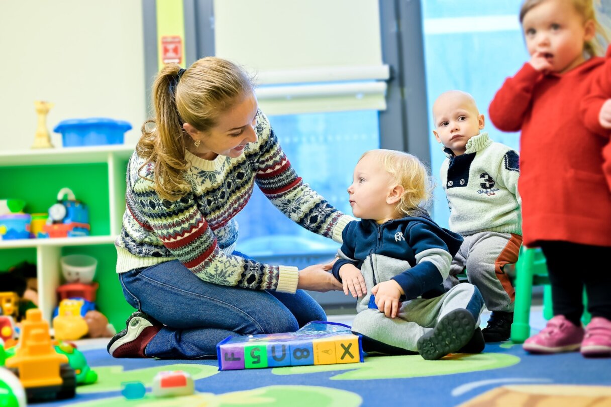 Daycare teacher interacting with children during playtime, helping them adapt to the time change.
