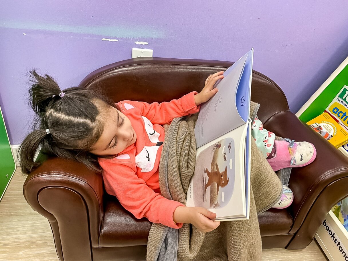 Little girl reading a book in a cozy daycare chair, unwinding during the time change transition