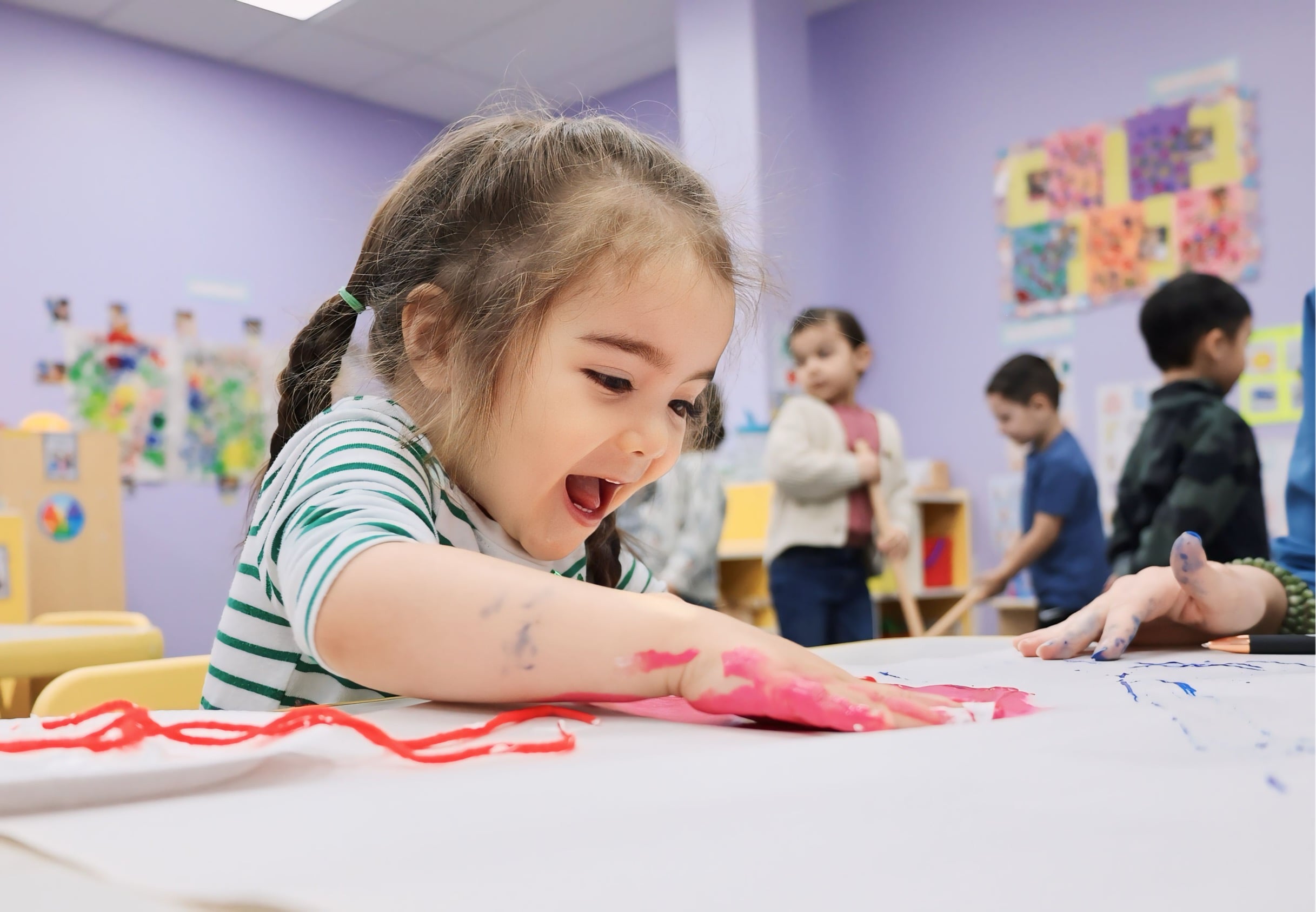 Young girl with a big smile painting with her hands in a classroom