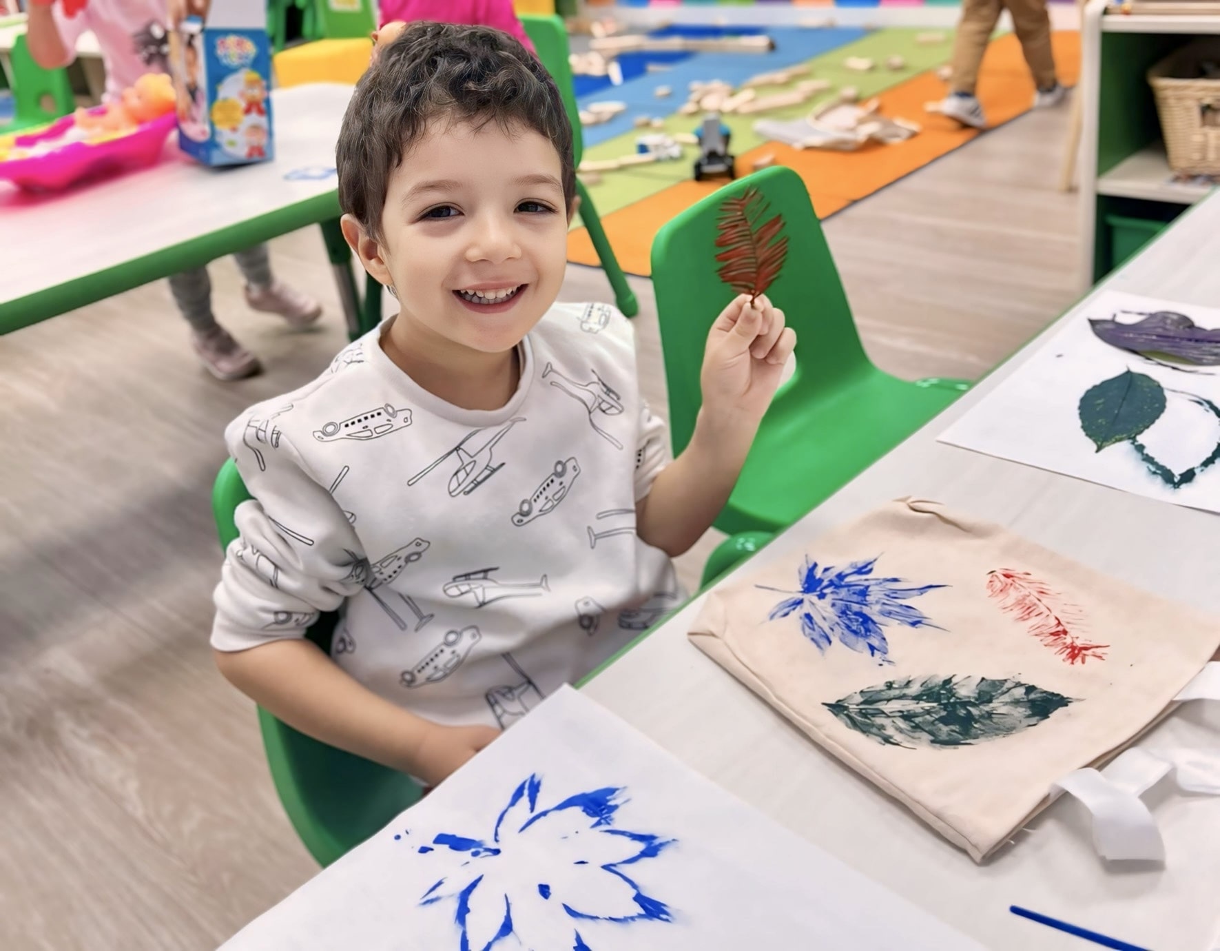 Smiling child displaying leaf stamp art on fabric, representing a creative eco-friendly hack for kids.