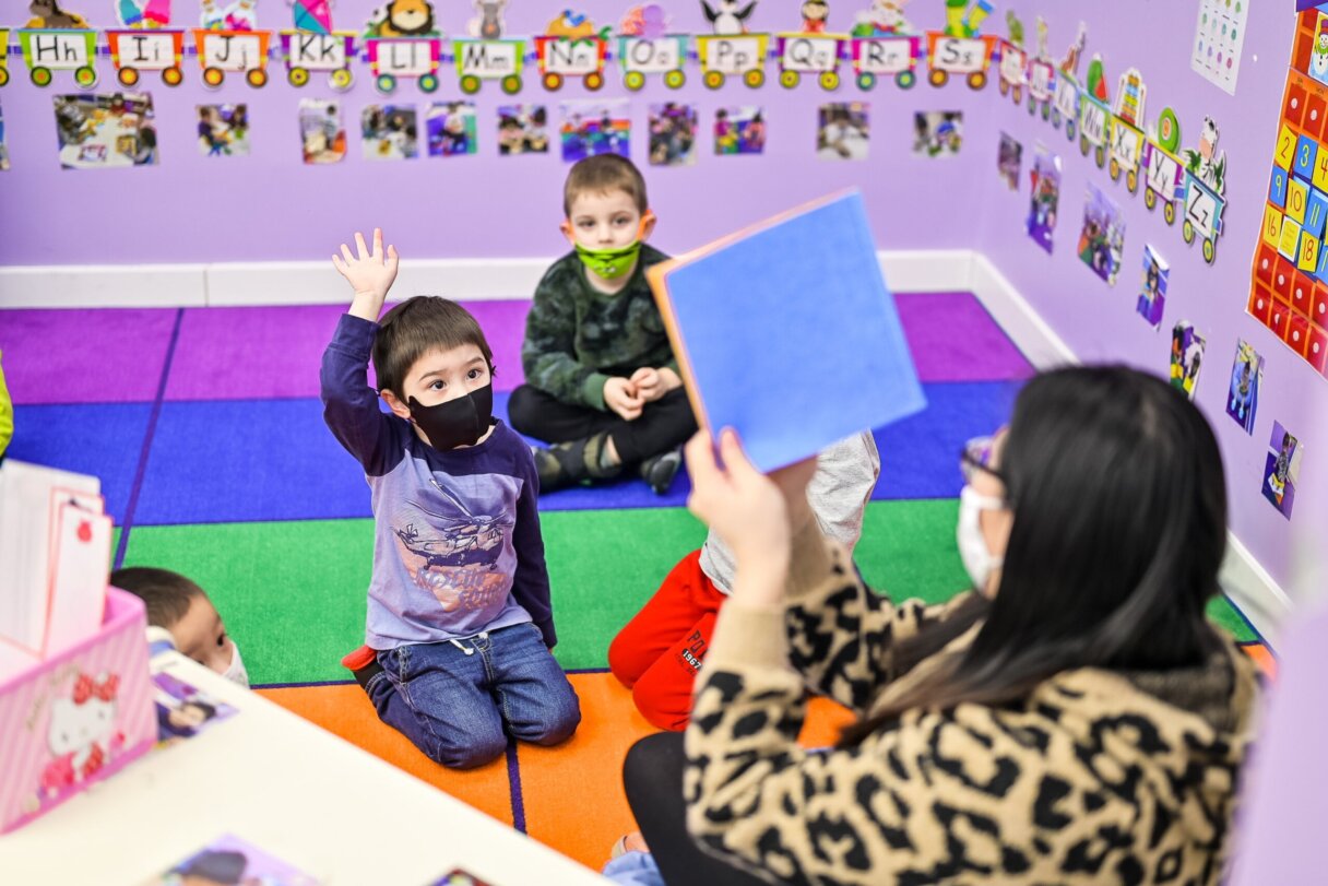Child raising hand during an interactive reading activity in a vibrant classroom setting