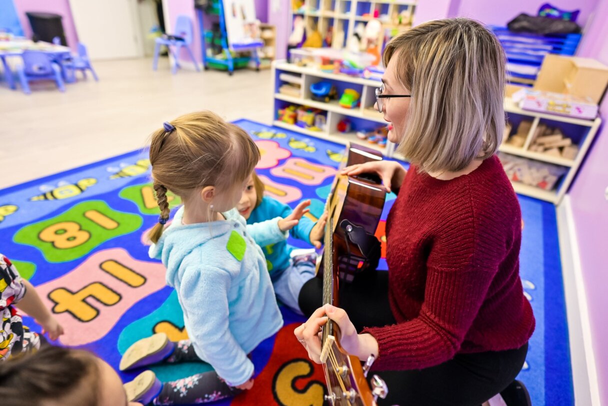Teacher with guitar showing chords to preschool children in a music class