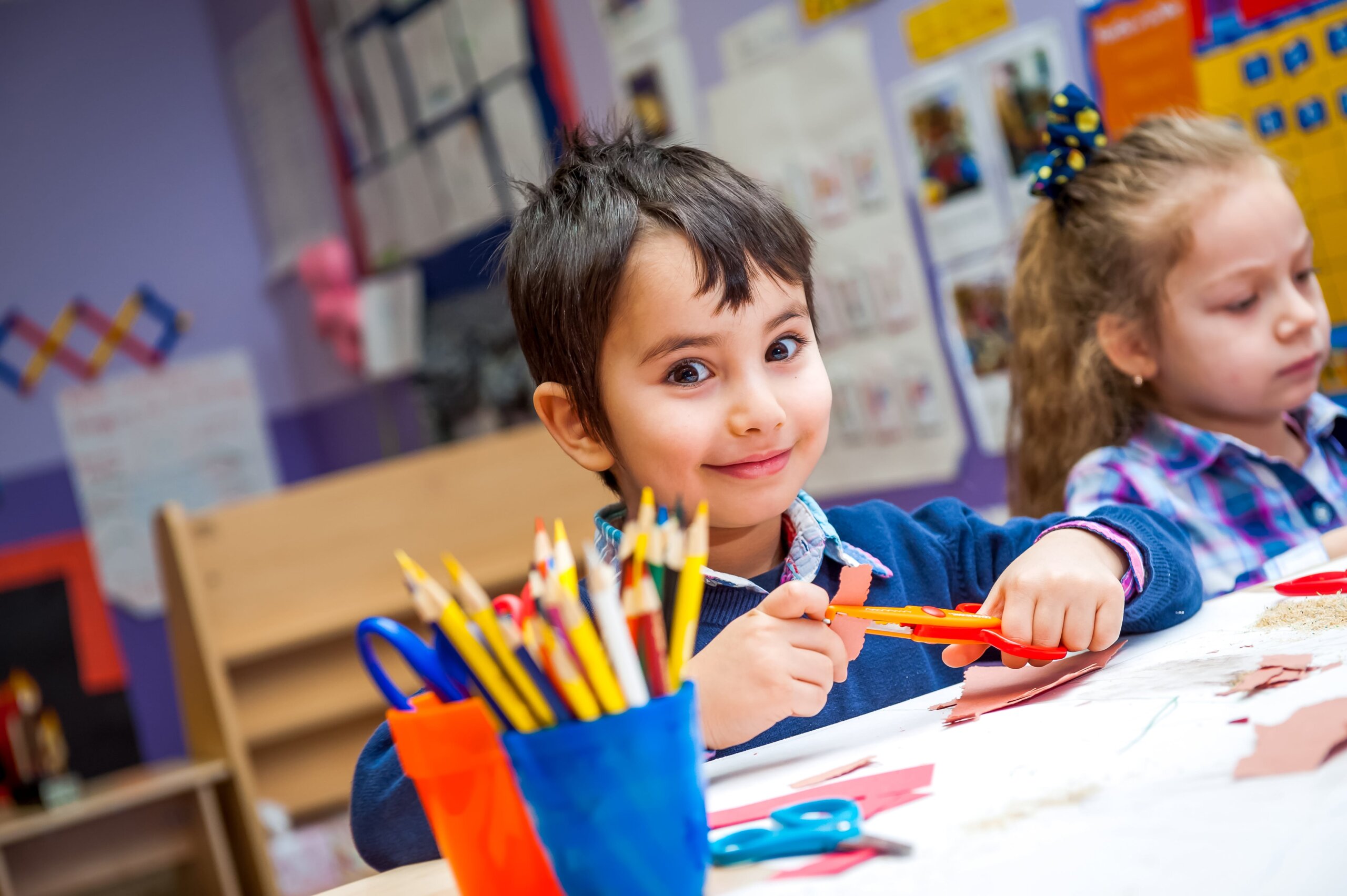 Child smiling while cutting paper in a classroom craft activity for spring