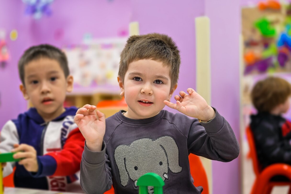 Preschool child gesturing during a language development activity in a colorful classroom