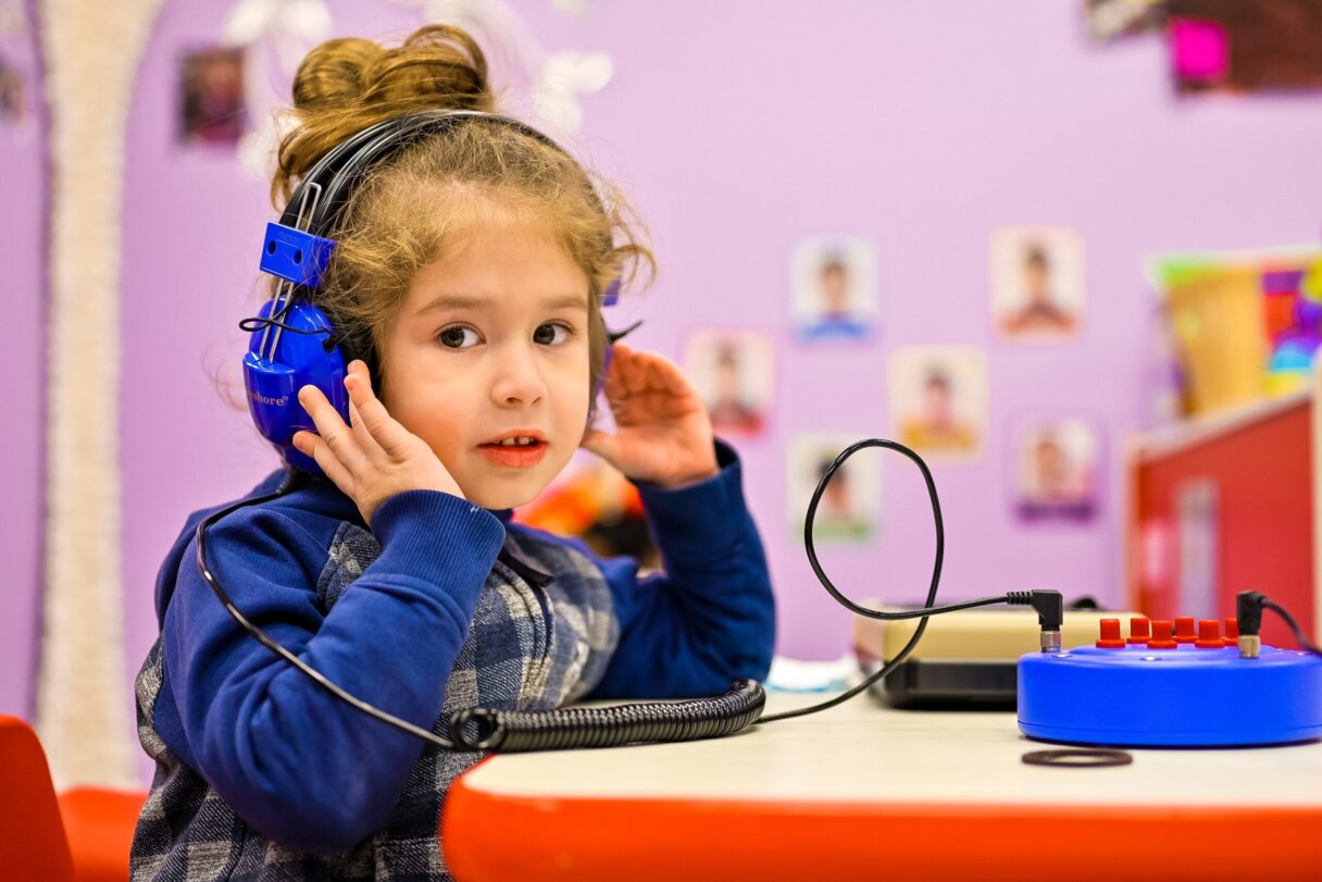 Preschool girl with blue headphones listening to music at daycare