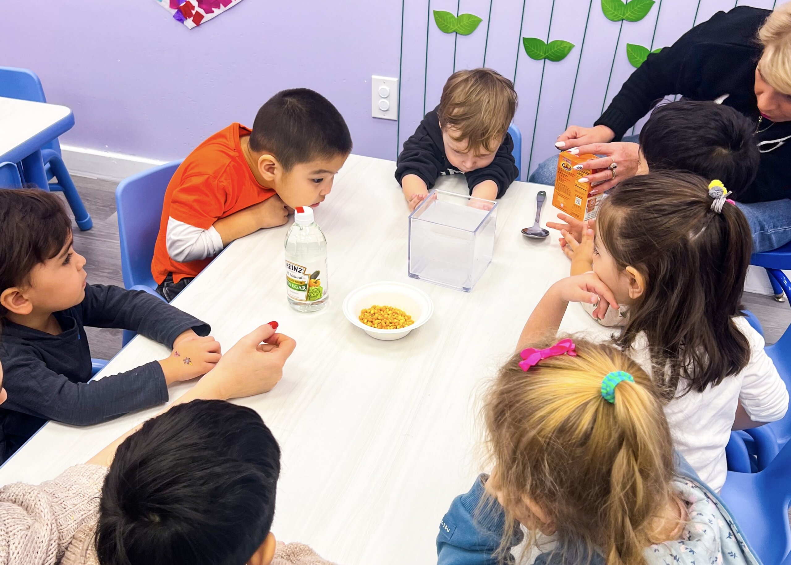 Preschool children attentively watching a vinegar and baking soda experiment at a classroom table