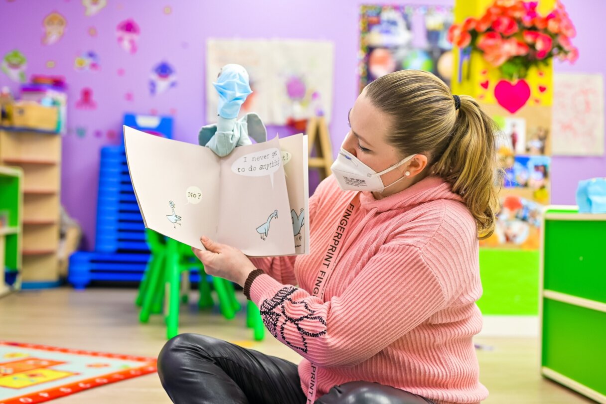 Teacher using a puppet to read a book to children  during the storytelling activity