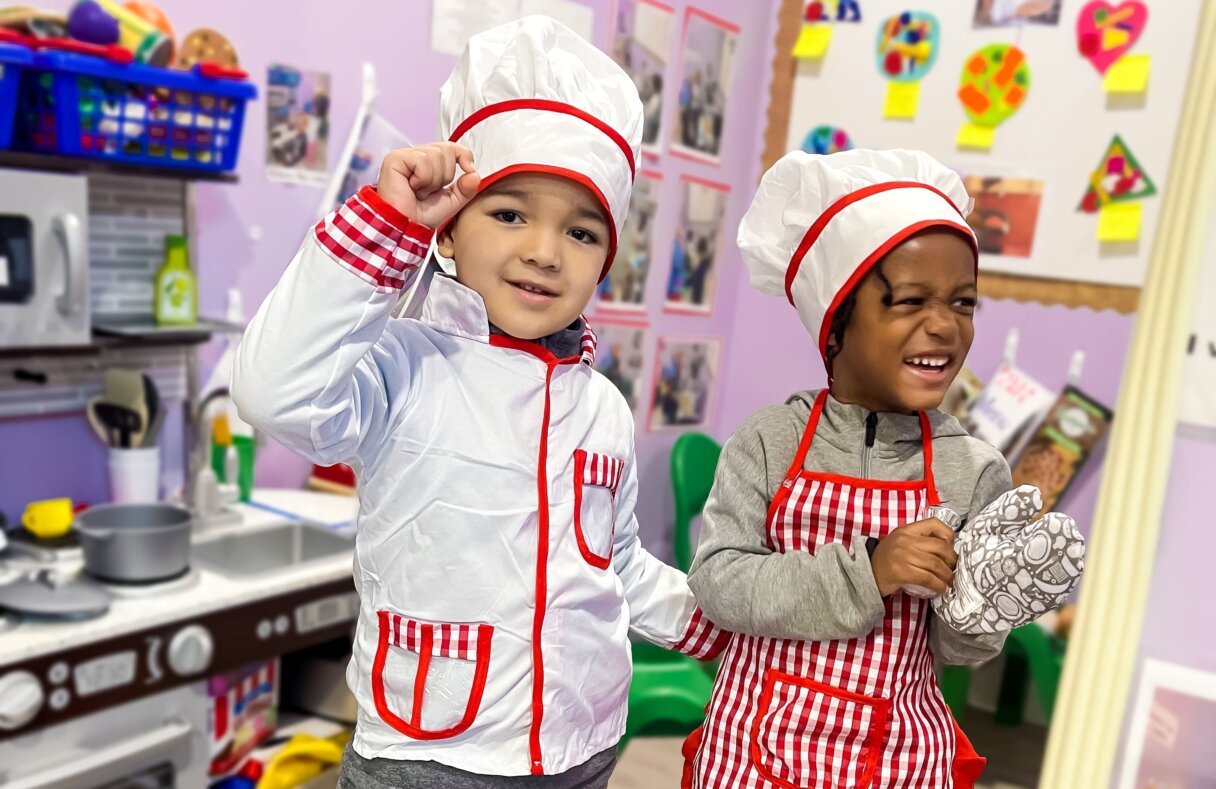 Two children dressed as chefs enjoy a playful cooking activity at Little Scholars Daycare.