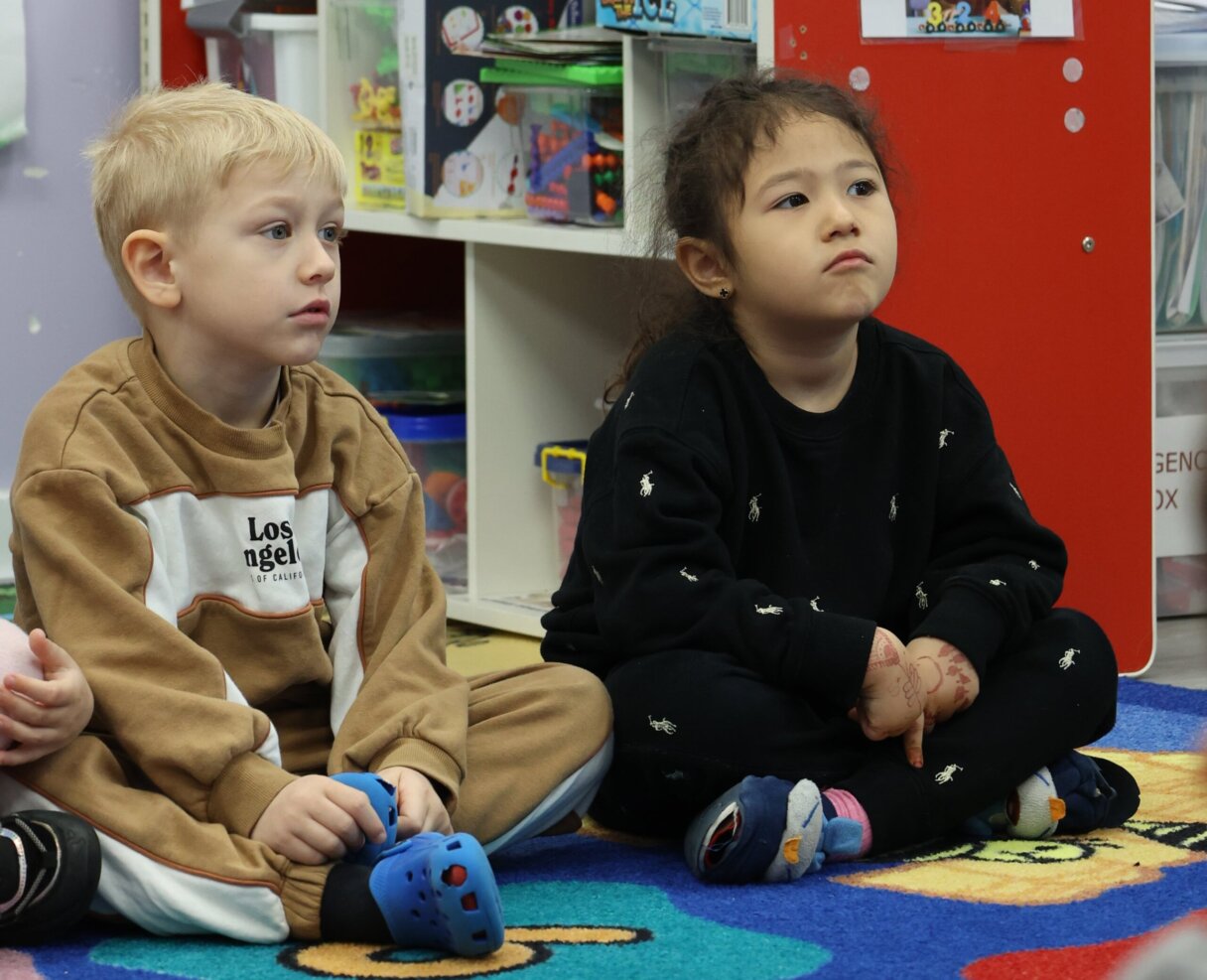 A young boy and girl sitting attentively during a story session at Little Scholars Daycare