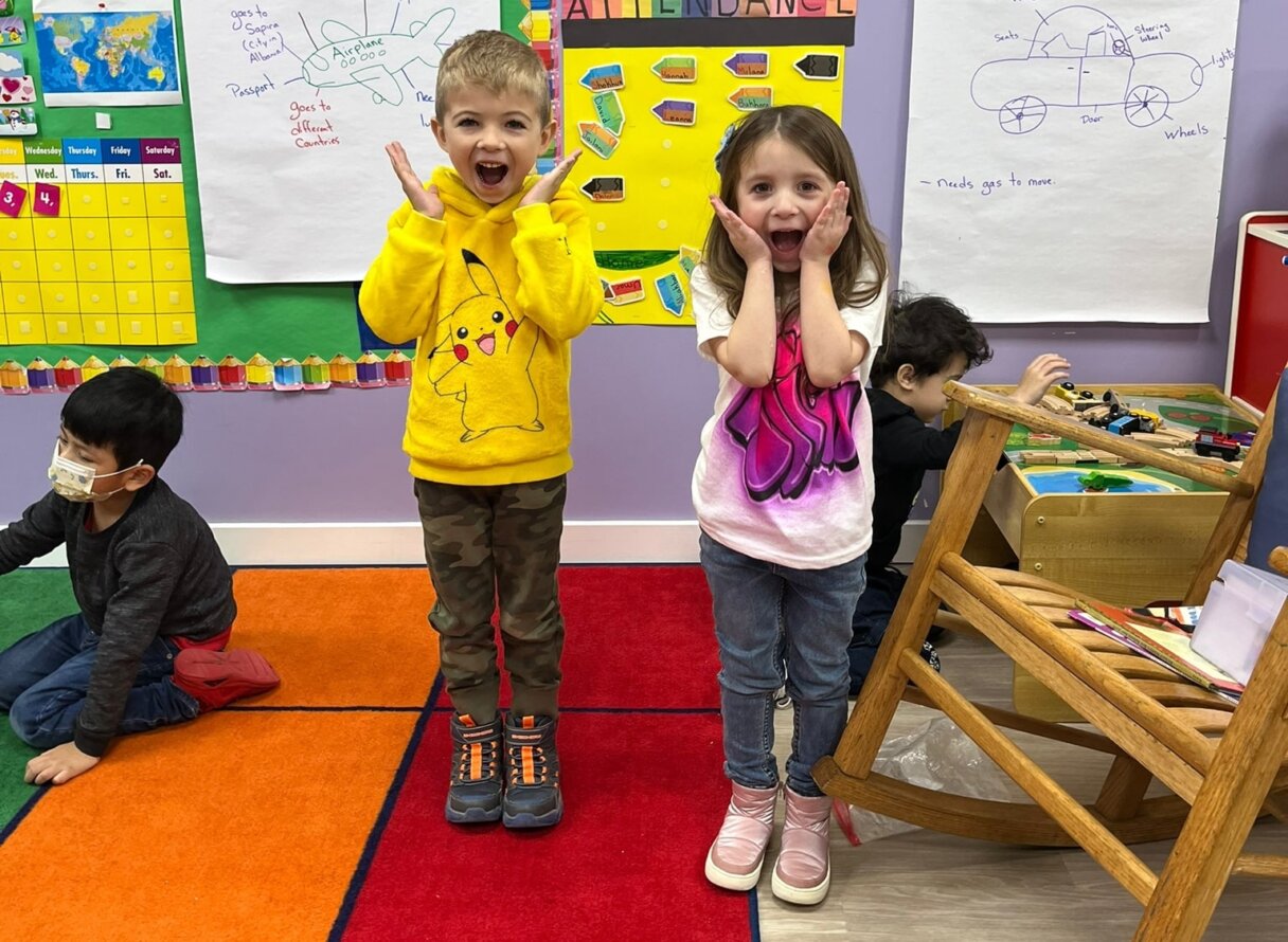 Two children express surprise and joy during a classroom activity at Little Scholars Daycare.